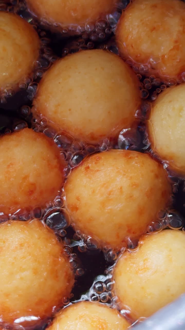Cooking tasty donuts with no hole in the center in a big amount of oil. Delicious sweets, no diet, unhealthy food. Close up. Vertical video.