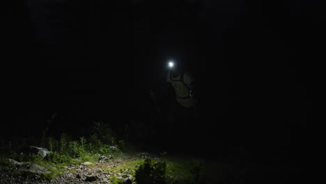 caminante subiendo una montaña en negro justo antes del amanecer, iluminando su camino con una linterna