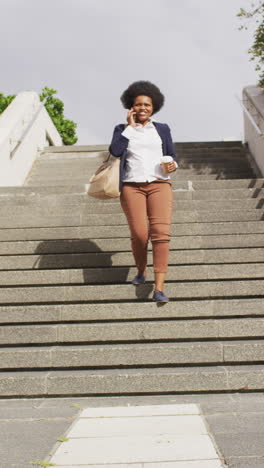 video: joyful african american woman descends stairs, coffee in hand, chatting on phone