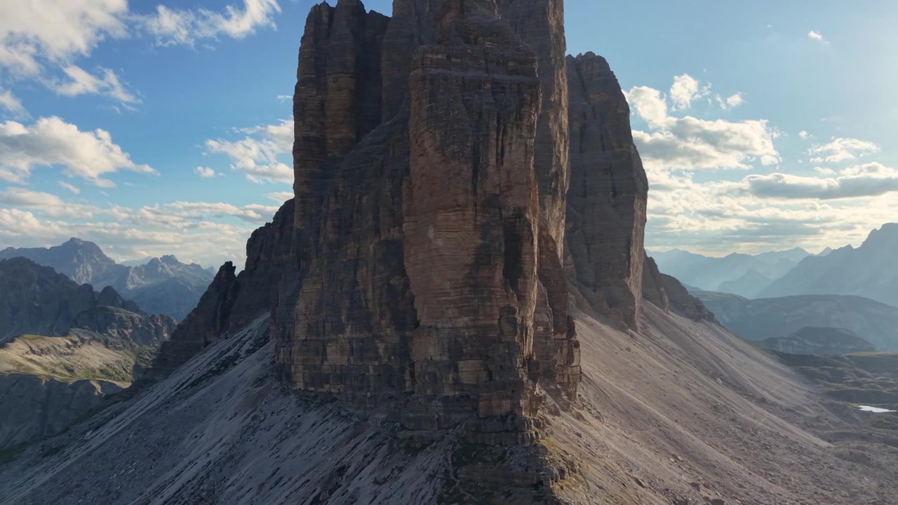 Cinematic drone view of the iconic Tre Cime di Lavaredo illuminated by warm golden hour light in the Dolomites, Italy