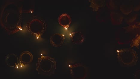 Fotografía-Cenital-De-Manos-Encendiendo-Lámparas-De-Aceite-Diya-Celebrando-El-Festival-De-Diwali-Sobre-Una-Mesa-Oscura