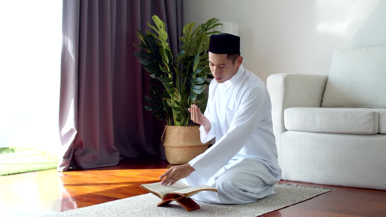 이슬람 옷을 입은 젊은 이슬람 남자가 꾸란을 읽고 기도하고 있습니다.