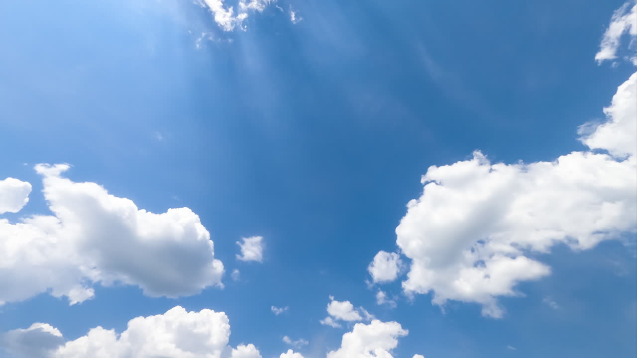 Beautiful sunrays coming through the light soft clouds in the blue summer sky. Timelapse low angle view.