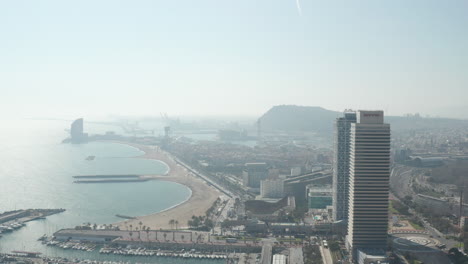 Aerial-panoramic-footage-of-city-at-seashore-against-sun.-Revealing-marina-with-moored-yachts-and-sailboats.-Barcelona,-Spain