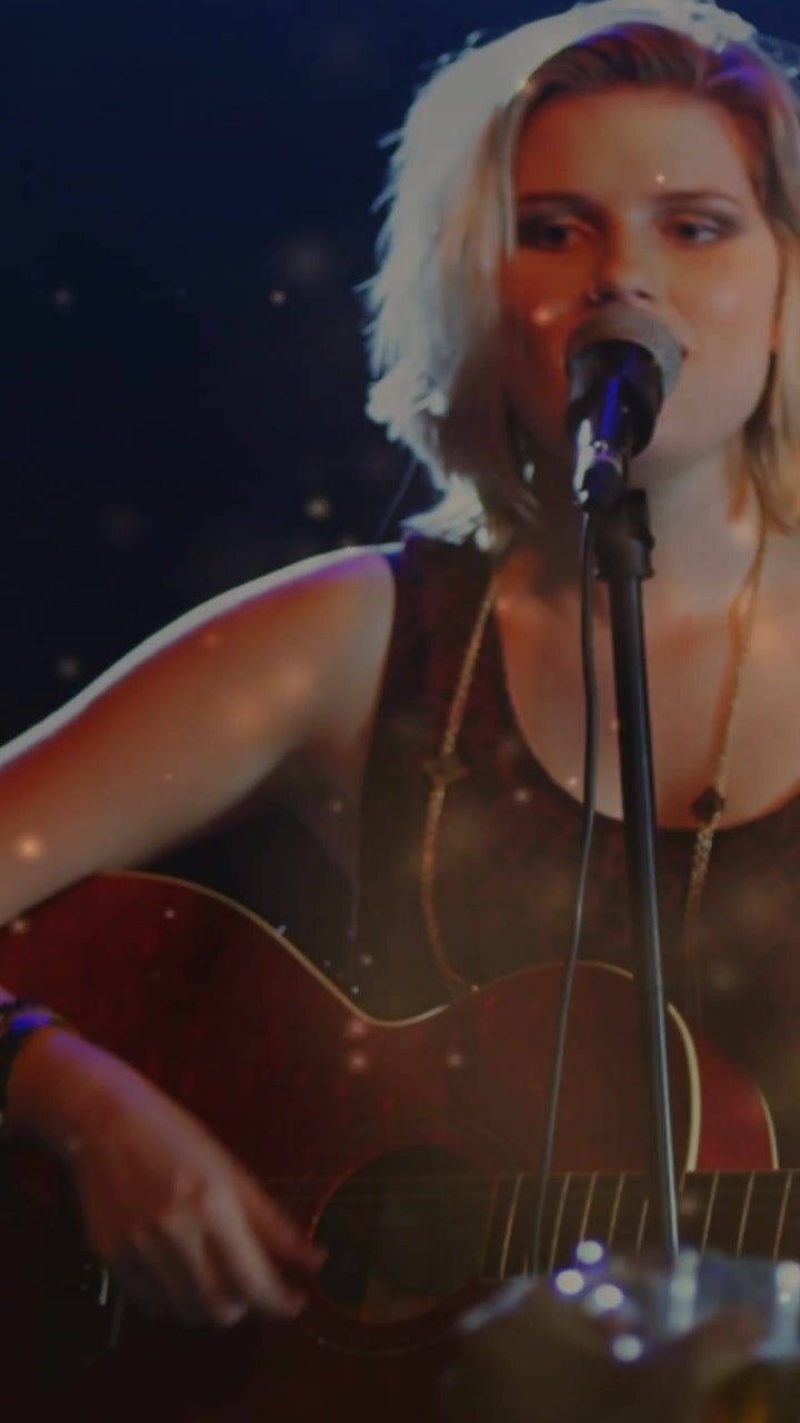 Video verticale: Un riflettore illumina un cantante che suona la chitarra, con bagliori di luce sul viso, mentre coinvolge i fan della musica.
