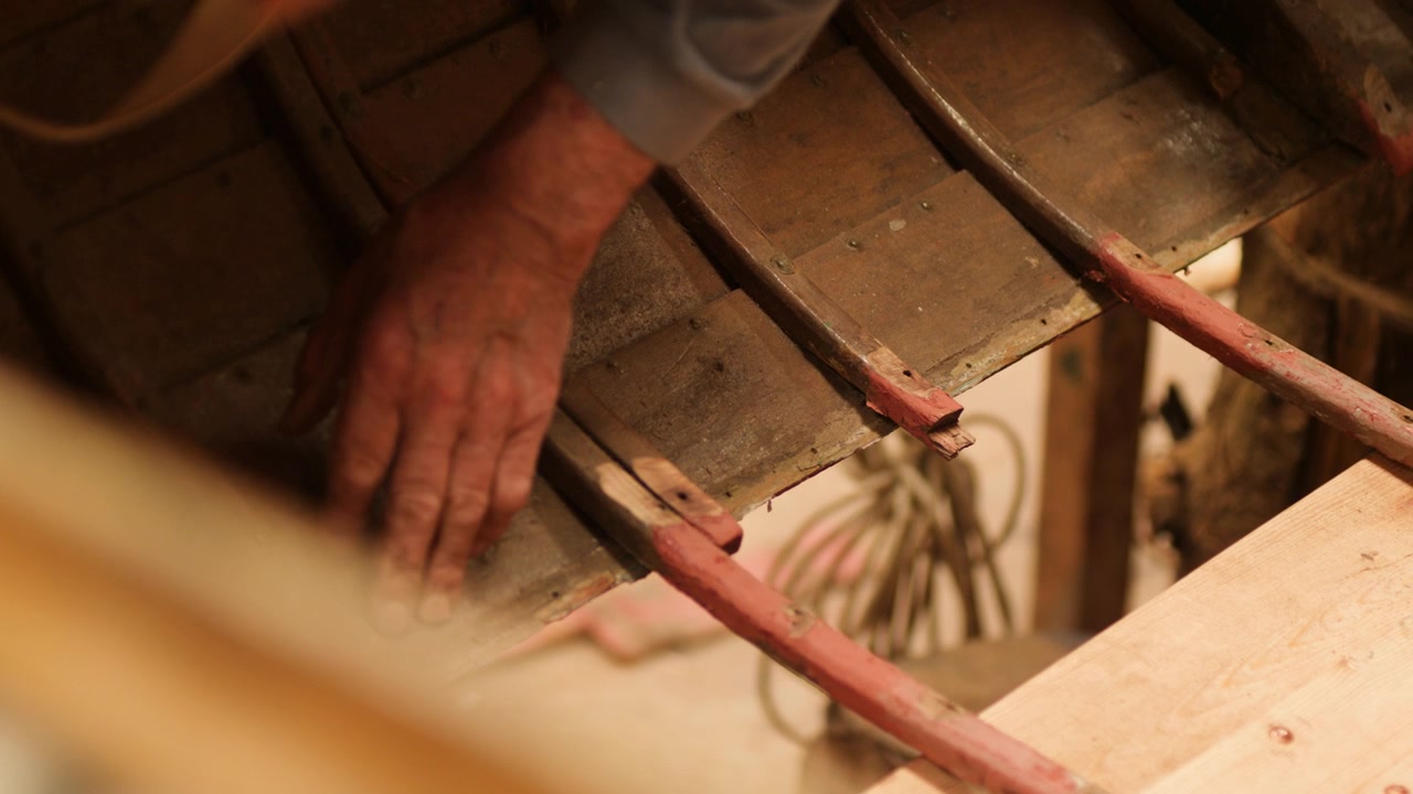 Carpenter inspecting hull of old clinker wood boat