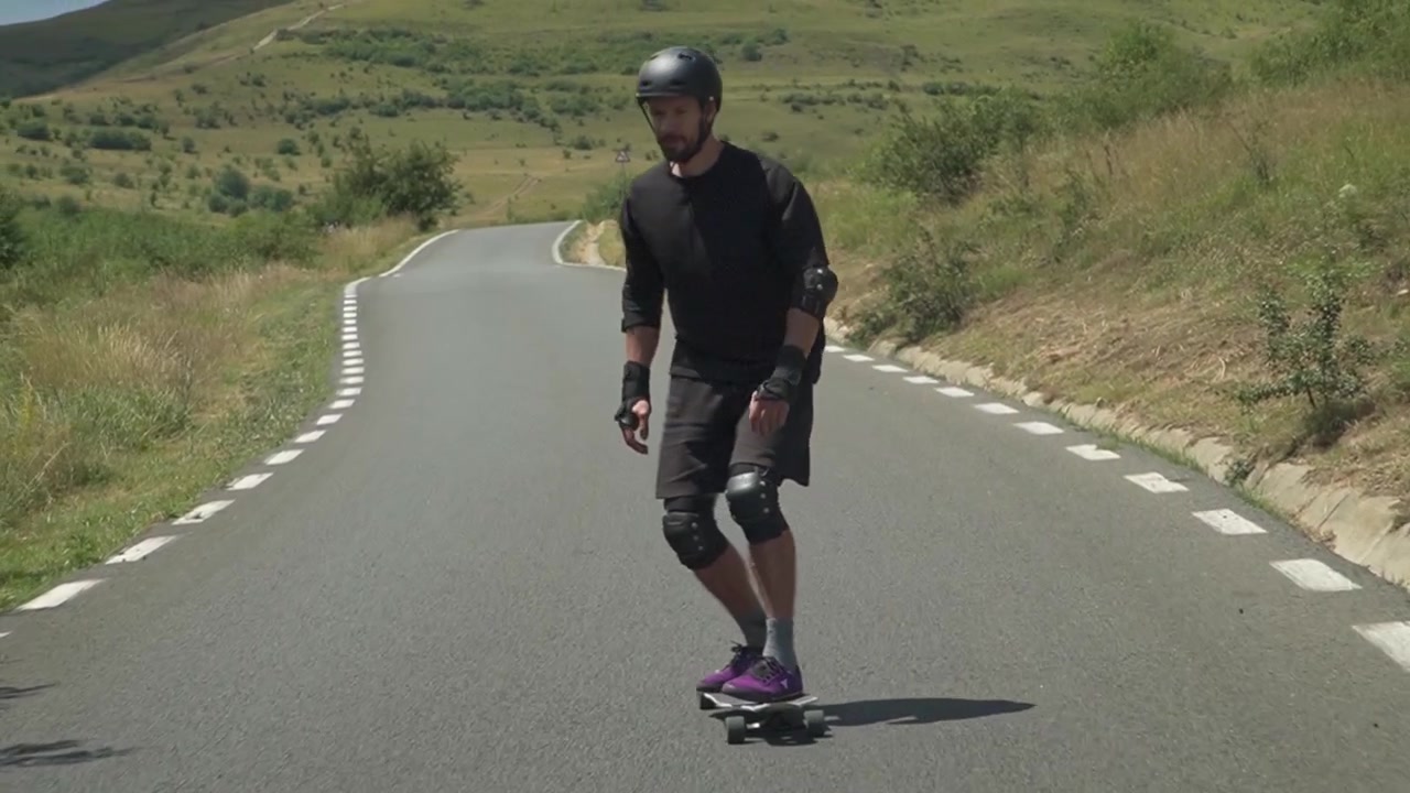 A skater in protective gear navigates a winding road under clear skies, showcasing balance and control.