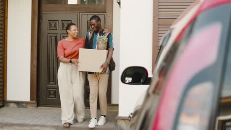 Joven-Sosteniendo-Una-Caja-Caminando-Con-Su-Madre-Hacia-El-Auto-Antes-De-Mudarse-A-Casa