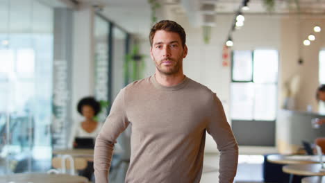 Portrait-Of-Serious-Businessman-Standing-In-Busy-Modern-Open-Plan-Office