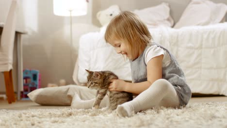 cute little girl sits on the floor and happily holds her favourite striped kitten. slow motion.