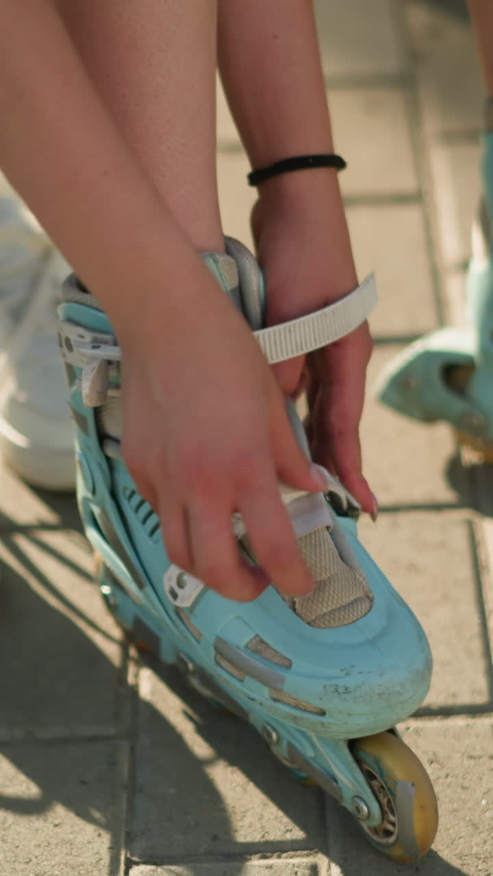 Partial view of individual adjusting roller skate strap on left leg while wearing black wrist band, white sneakers lying in background, with greenery in the background