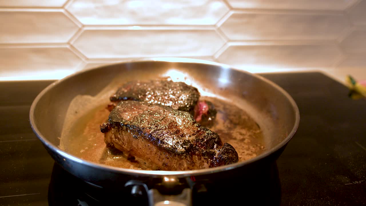Nahaufnahme von Rindersteaks, die in Butter auf einem Küchenherd mit warmer Beleuchtung brutzeln
