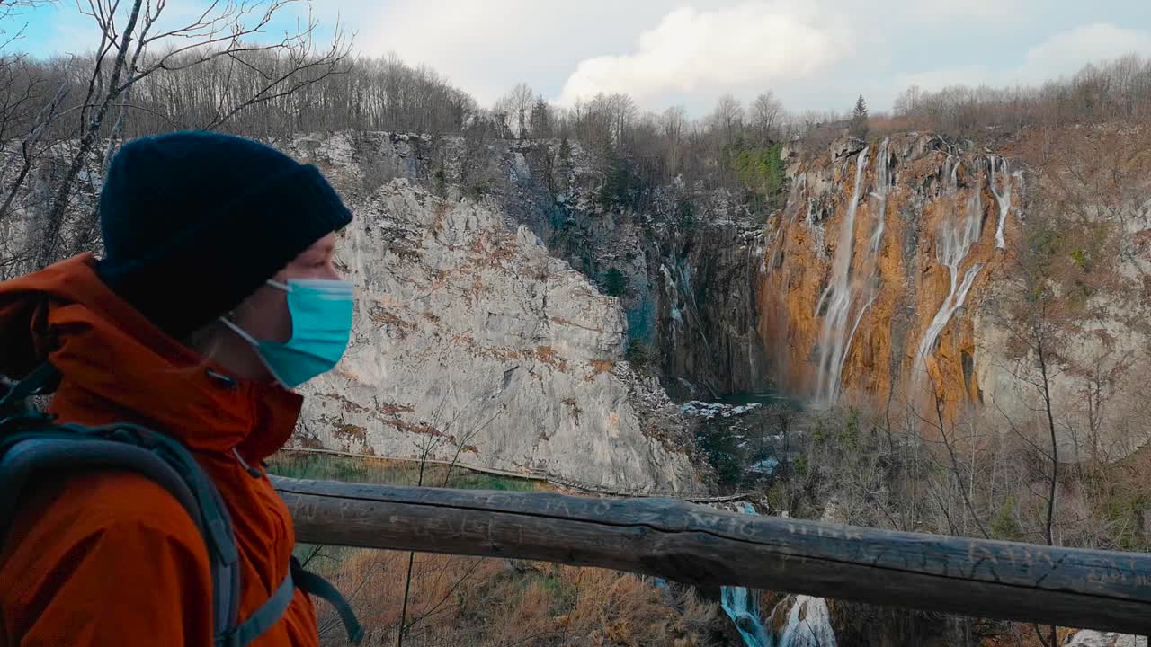 In a Croatian national park, a girl, wearing an op mask, navigates the landscape, embodying safety measures while exploring nature's beauty in the pandemic era