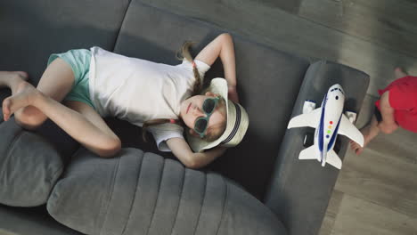 preschooler girl lies on couch near brother playing with toy