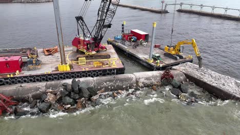 Using-a-grapple,-a-crane-moves-pieces-of-riprap-to-build-up-a-pier-in-Algoma,-WI-on-Lake-Michigan