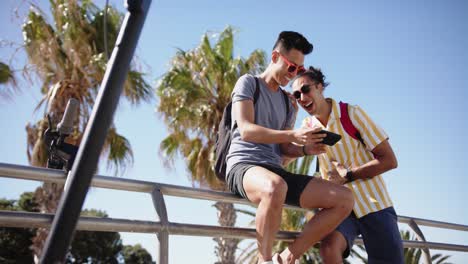 happy diverse gay male couple using smartphone at promenade, slow motion