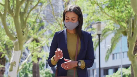 African-american-woman-wearing-face-mask-disinfecting-hands-in-the-street