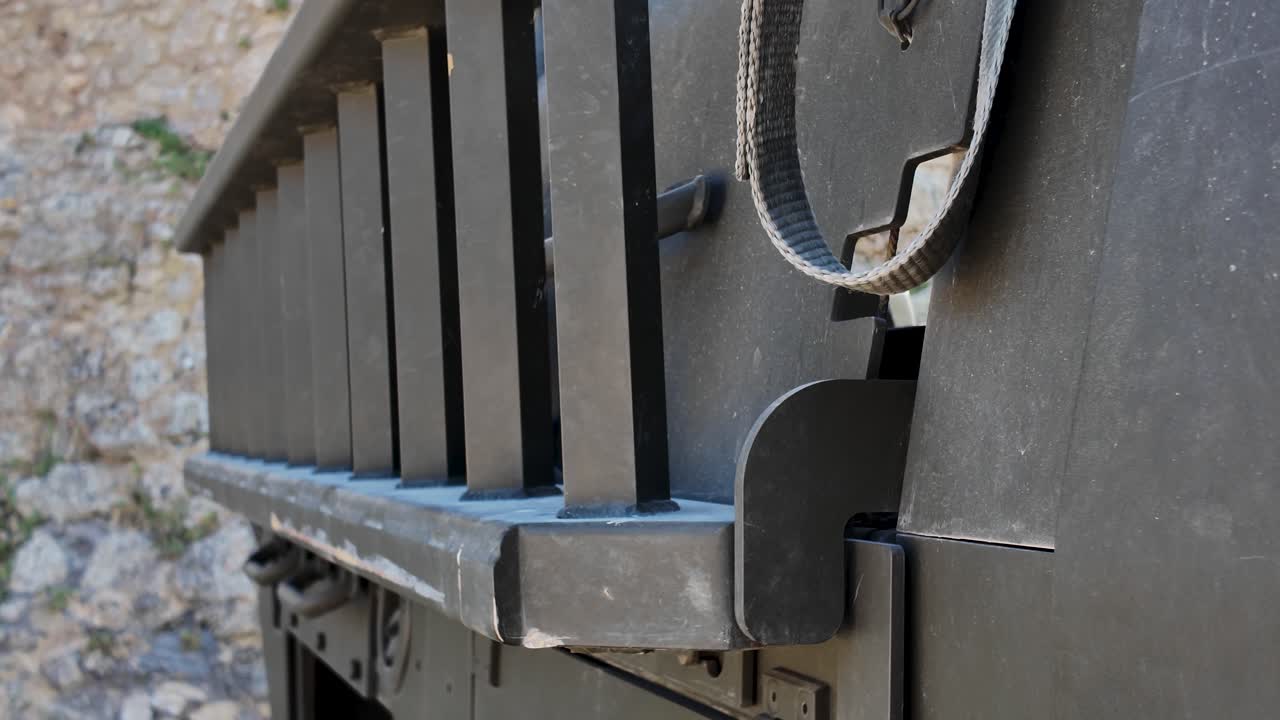 Close up of securing strap hanging on the front grill of a military vehicle, suggesting preparation for transport or deployment