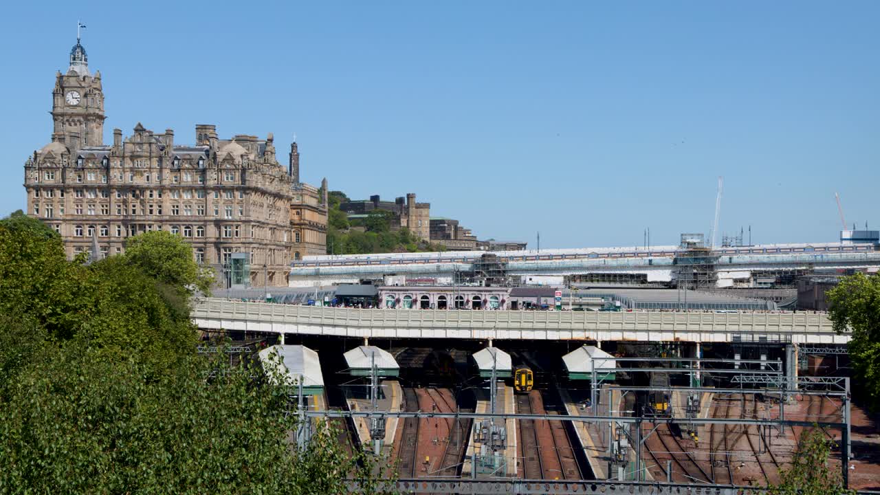 Passenger train travels across Waverley Bridge, historic architecture, clear daylight, wide static shot