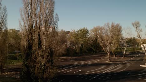 aerial dolly shot of an empty parking lot with trees during the covid-19 pandemic. the camera is moving from left to right revealing the bratislava castle in the background behind the trees.