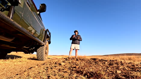 field guide shows elephant dung content to guests, low pov next to safari truck