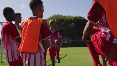 Video-Einer-Gemischten-Gruppe-Männlicher-Fußballspieler,-Die-Sich-Auf-Dem-Spielfeld-Aufwärmen,-Stehen-Und-Ihre-Beine-Ausstrecken