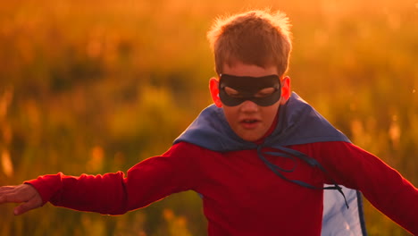 un niño con disfraz de superhéroe y máscara corriendo por el campo al atardecer soñando y fantaseando.