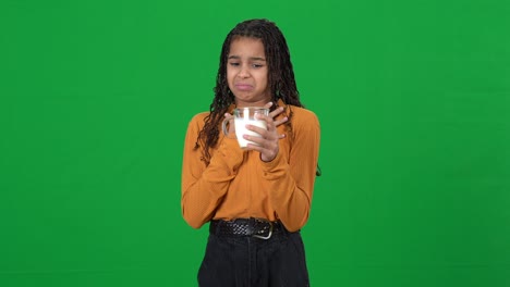 Portrait of dissatisfied teen girl with disgust facial expression holding milk in cup closing nose posing on green screen. Adolescent African American teenager with dairy at chromakey background.