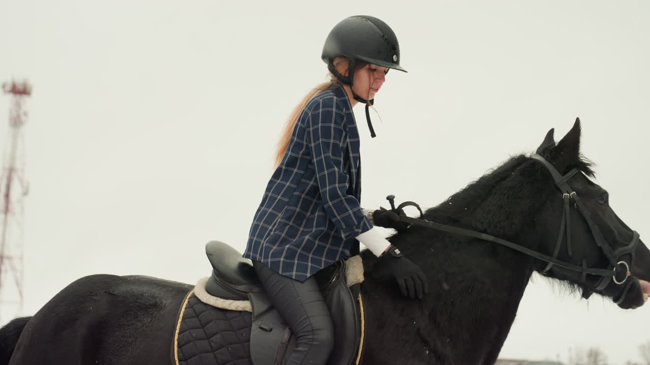 Donna su cavallo nero, primo piano di lezione di equitazione che mostra il cavaliere con casco che tiene le redini con espressione concentrata, torri urbane sullo sfondo, dettagli di sella e briglia visibili, luce invernale calma, addestramento