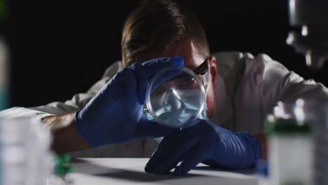 médico caucásico de sexo masculino con máscara facial y guantes inspeccionando la placa de petri