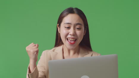 close up of happy asian business woman celebrating using laptop computer on green screen in the studio