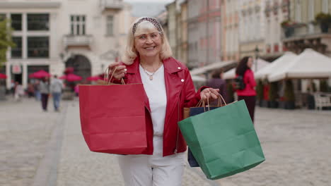 mujer mayor feliz adicta a las compras consumidor después de la venta de compras con bolsas llenas caminando por la calle de la ciudad