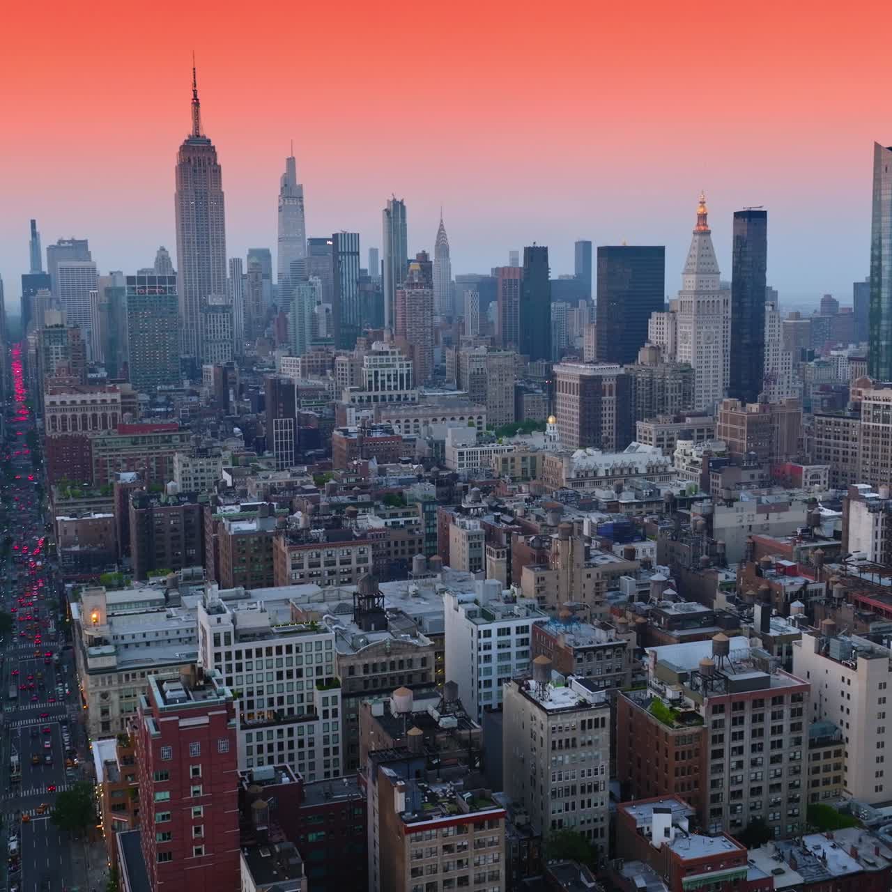 Splendid panorama of beautiful New York at sun down. Broad street full of cars having red lights on moving by. Pink sky background