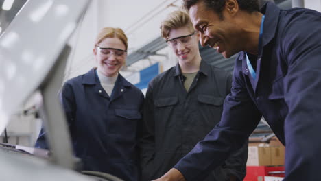 male tutor with students looking at car engine on auto mechanic apprenticeship course at college