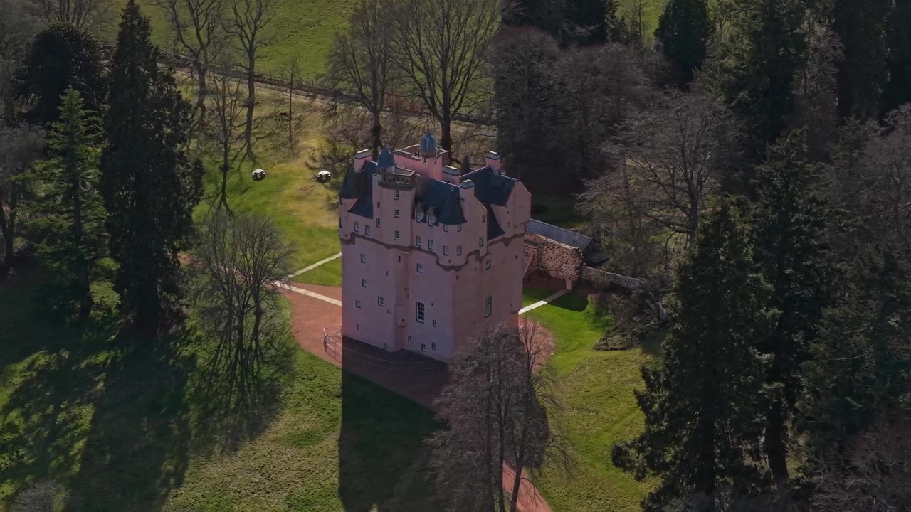 Piękne ujęcia z lotu ptaka przedstawiające ikoniczny różowy bajkowy zamek Craigievar w szkockich wyżynach, otoczony leśnymi drzewami.