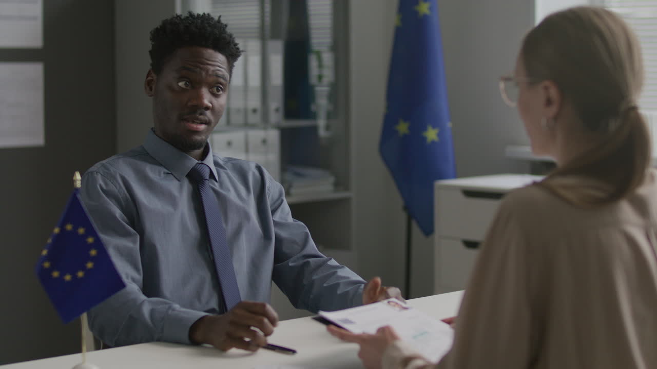 Afroamerický žadatel o vízum hovoří s konzulárním úředníkem na velvyslanectví EU.
