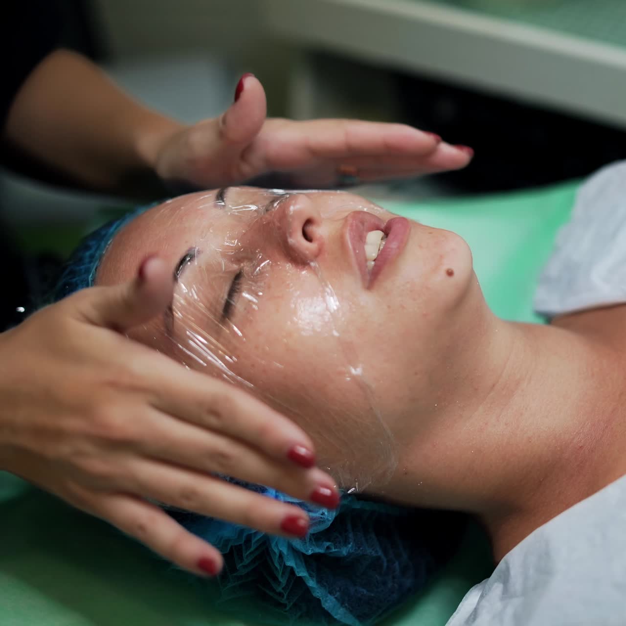 Beautician covering female client's face with cellophane. Cosmetologist preparing a woman for cosmetic skincare procedures. Close up