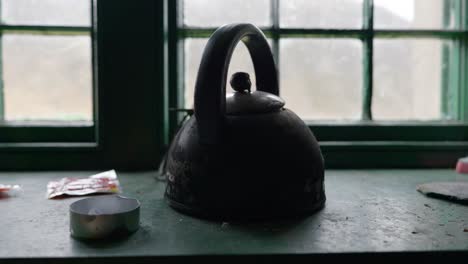 slow panning shot of an old kettle sitting on a windowsill in a remote scottish highland mountain shelter