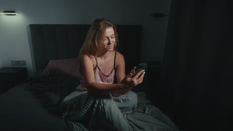 woman using phone in bed at night