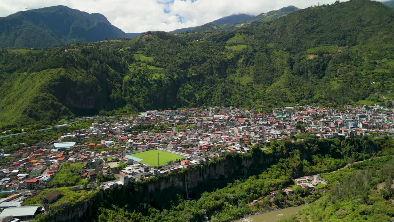 Drone sorvola la città di Baños de Agua Santa rivelando il paesaggio urbano incastonato tra imponenti montagne verdi e scogliere ripide in una drammatica valle andina del Tungurahua, Ecuador.