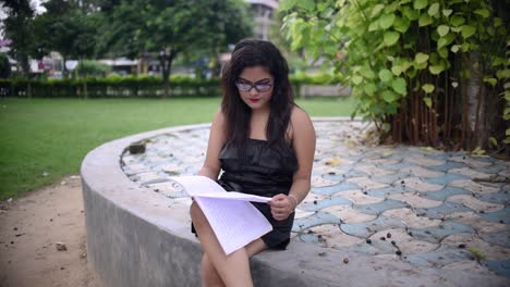 a hot asian girl is studying under a tree inside university college campus ground, reading a book