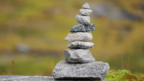 a small tower of carefully balanced stones sits on a rock, framed by the greenery and rocks of a natural setting