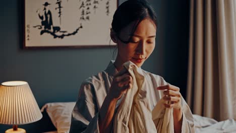 woman gently holding cherished clothing item, bathing in soft lamp light, embodying nostalgic sentiment and quiet emotional reflection within peaceful, intimate home interior