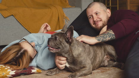 couple caressing her bulldog dog liying on the floor in living room