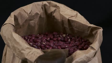 los frijoles secos de adzuki giran en una bolsa de papel contra un fondo negro, primer plano