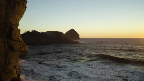 Ocean-waves-crash-on-sandstone-cliffs-glowing-orange-from-sunset,-Cape-Kiwanda,-Oregon-Coast