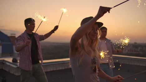 Young-women-on-the-roof-moves-a-dance-with-her-friends-on-a-summer-evening-with-big-bengal-light.-It's-a-pleasure-sunset-before-night.