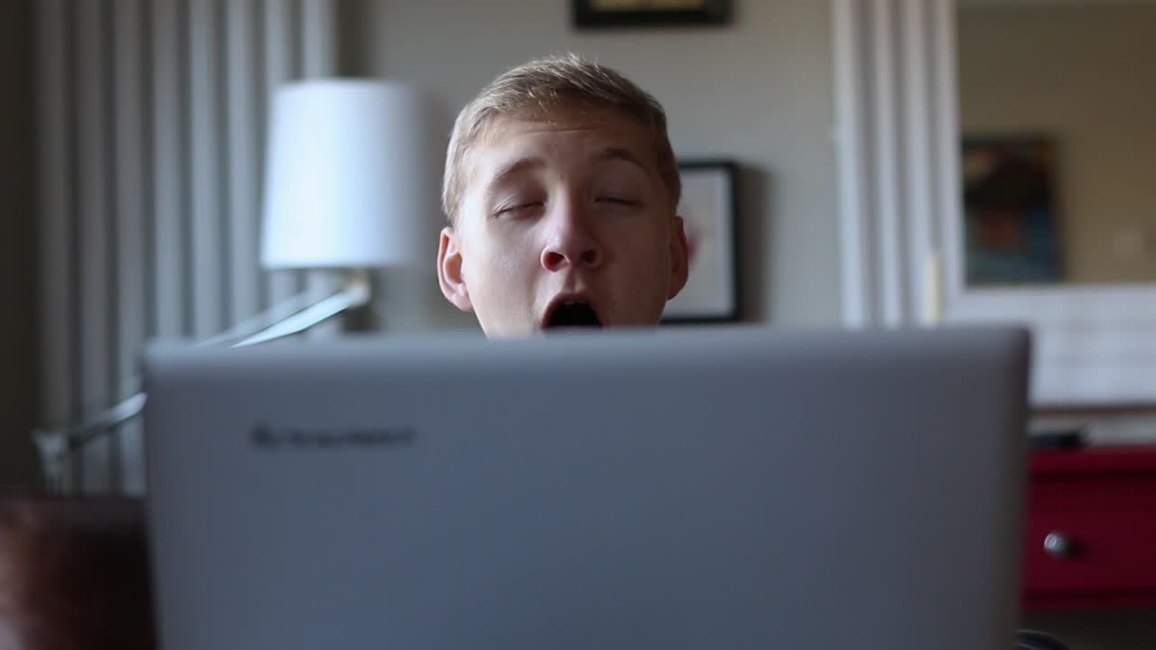 Drowsy Teenager Yawns While Surfing on His Laptop