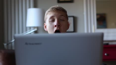 drowsy teenager yawns while surfing on his laptop