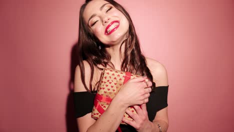 brunette happy woman open her present with confetti in pink background wear black dress
